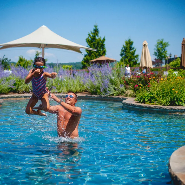 Young girl midair as her father throws her in pool.