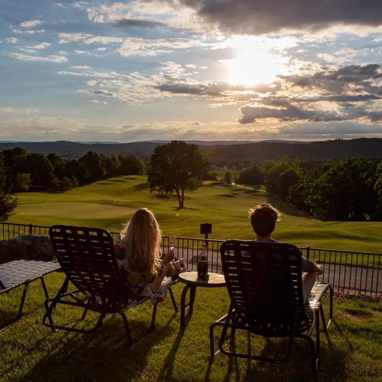 Woman and man sitting in lounge chairs looking at a sunset.