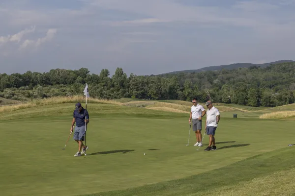 Golfers putting on Ballyowen Golf Course with mountains in background.