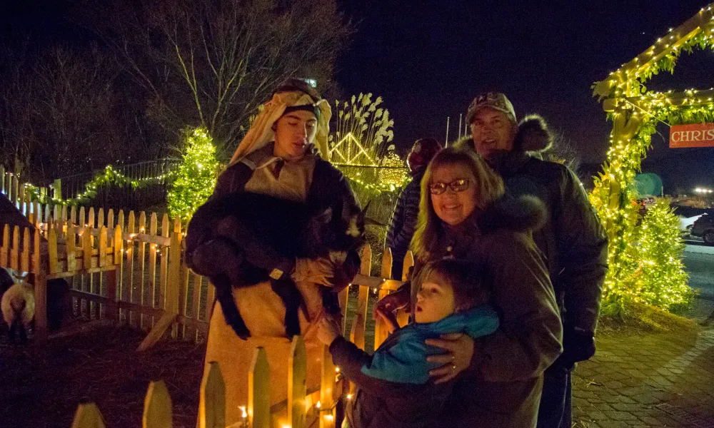 Grandparents with their grandchild and shepherd holding a goat in a live nativity scene.